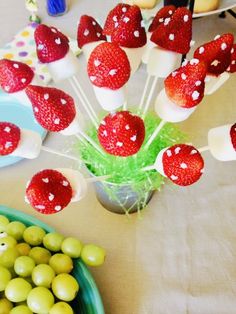 strawberries and green olives are arranged on skewers in front of a bowl of grapes