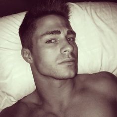 a shirtless man laying in bed with his eyes open and hair sticking out from the side