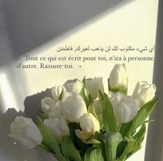 a vase filled with white tulips sitting on top of a table next to a wall