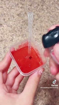 a person holding a container with red liquid in it and a black object sticking out of it