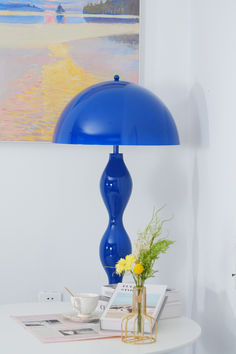 a blue lamp sitting on top of a table next to a vase with yellow flowers