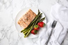 a white plate topped with salmon and asparagus next to strawberries on a table