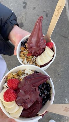 two bowls filled with ice cream and fruit on top of each other next to a person's hand