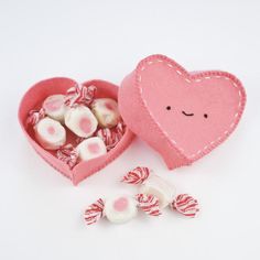 a heart shaped box filled with candy and marshmallows on a white surface