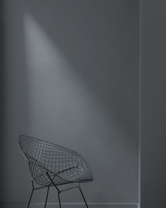 an empty chair in front of a gray wall with light coming through the window on it