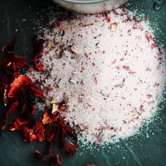 a bowl filled with white powder next to red flowers on top of a green table