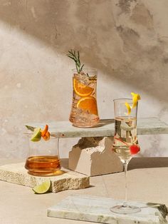 two glasses filled with different types of drinks on top of a wooden table next to a stone slab