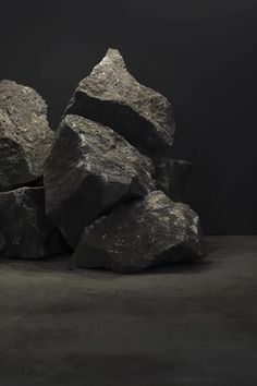 a pile of large rocks sitting on top of a cement floor next to a black wall