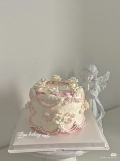 a white cake sitting on top of a table next to an angel figurine