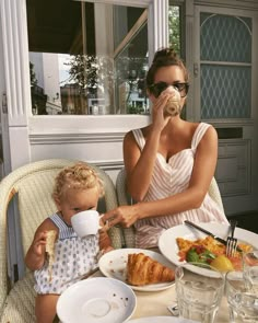 a woman sitting at a table with a child eating food and drinking from a cup