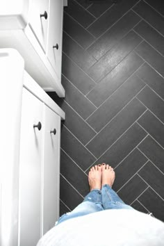 a person standing on the floor in front of a white cabinet and black tiled wall