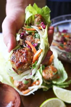 a person holding up a meatball sandwich with lettuce, carrots and slaw