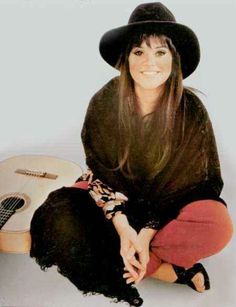 a woman sitting on the ground with a guitar in her lap and wearing a black hat