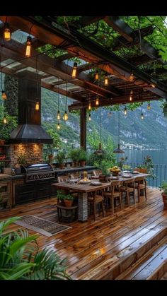 an outdoor kitchen and dining area overlooking the water with lights hanging from it's roof