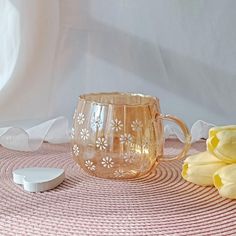 a glass mug sitting on top of a table next to yellow flowers