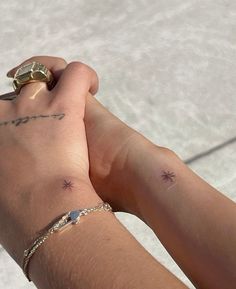 two people holding hands with tattoos on their arms and wristbands, both wearing gold rings