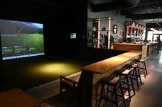 a bar with several stools in front of it and a large screen on the wall