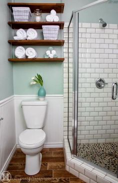 a white toilet sitting inside of a bathroom next to a walk in shower and wooden shelves