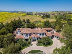 an aerial view of a large home with trees and mountains in the background, surrounded by greenery