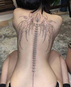 a woman sitting on the floor with her back turned to show an intricate tattoo design