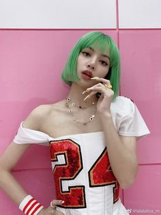 a woman with green hair is posing in front of a pink wall and eating a donut