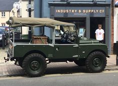 a green jeep parked in front of a building with a man standing next to it