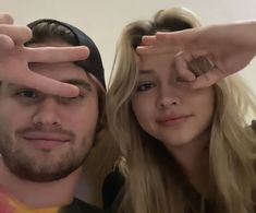 a man standing next to a woman holding their hands up in the shape of two fingers