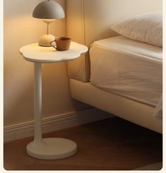 a white table with a cup on it next to a bed and lamp in the corner