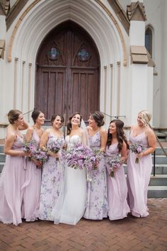 a group of women standing next to each other in front of a church with purple flowers