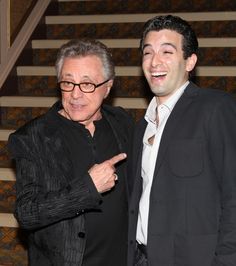 two men standing next to each other in front of a stair case with one pointing at the camera