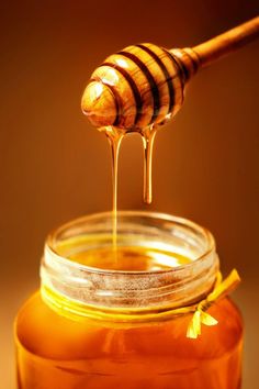 honey dripping from a wooden spoon into a jar