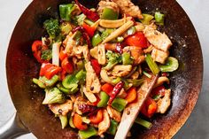 a wok filled with chicken, peppers and broccoli on top of a table