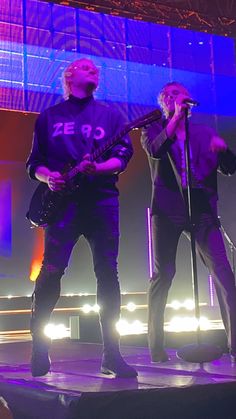 two men standing on stage with guitars in their hands