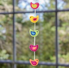 three colorful birds hanging from a wire next to a window