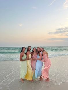 four women standing in the water at the beach with their arms around each other and smiling