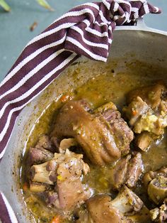 a pot filled with meat and vegetables on top of a table next to a striped cloth