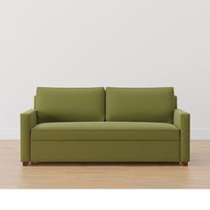 a green couch sitting on top of a hard wood floor next to a white wall