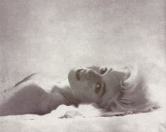 an old photo of a woman laying on her stomach in the middle of white sheets