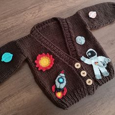 a knitted jacket with patches and buttons on it sitting on a wooden floor next to a pair of scissors