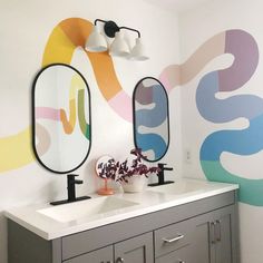 a bathroom with two sinks, mirrors and a wall painted with colorful swirls on it