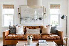 a living room with brown leather couches and pillows on the coffee table in front of two windows