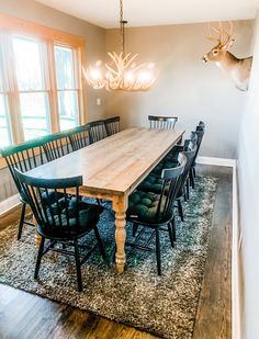 a dining room table with black chairs and a deer head on the wall behind it