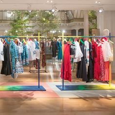 a clothing store with clothes hanging on racks and colorful rugs in front of them