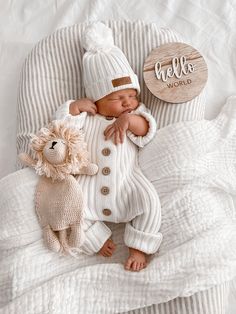 a baby sleeping next to a stuffed animal on top of a white blanket with a hello world sign