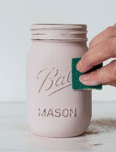 a person is cleaning a mason jar with a green sponge to clean the paint off