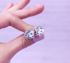 a person's hand with two playing cards earrings on it, and the fingers are holding them