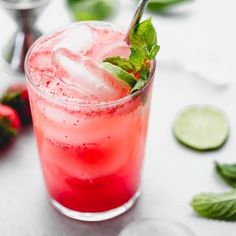 a glass filled with ice and some strawberries next to minty garnish