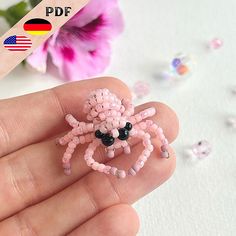 a small pink spider brooch sitting on top of a persons hand next to flowers