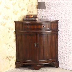 a wooden cabinet with a lamp on top of it next to a wallpapered wall