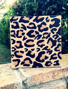 an animal print square box sitting on top of a stone wall next to some bushes